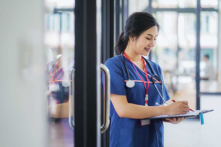 A medical practitioner in a navy uniform, holding a clipboard which she is using to take notes. She is stood in a corridor.