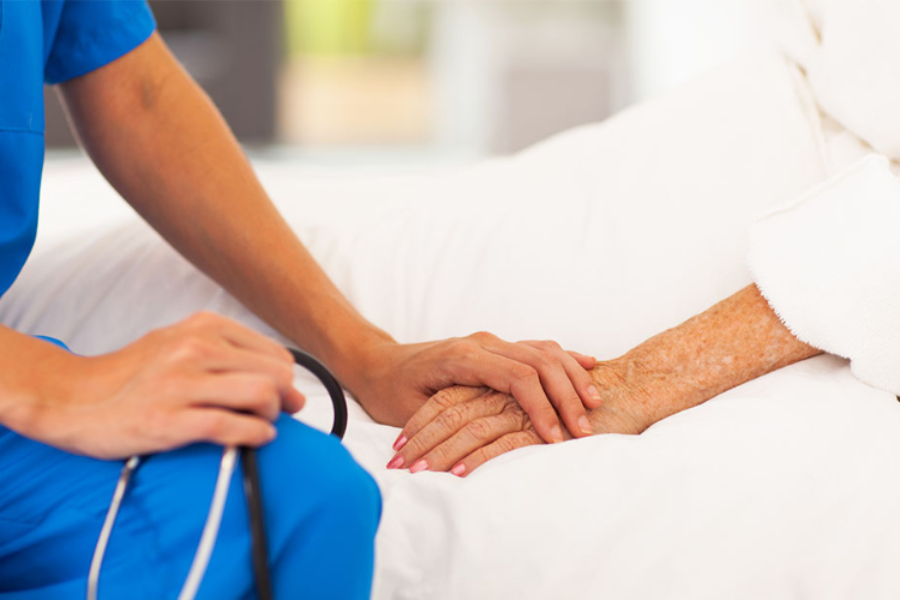 Close up of hands - nurse holding hand of female patient in bed