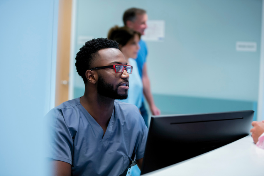 Male health worker looking at computer screen at reception desk.
